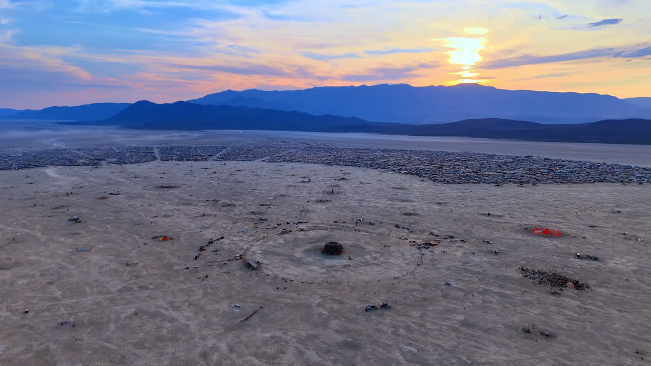 Aerial Dusk View Over the Playa at Burning Man. The playa stretches toward distant mountains as dusk colors blend into the sky above the festival grounds