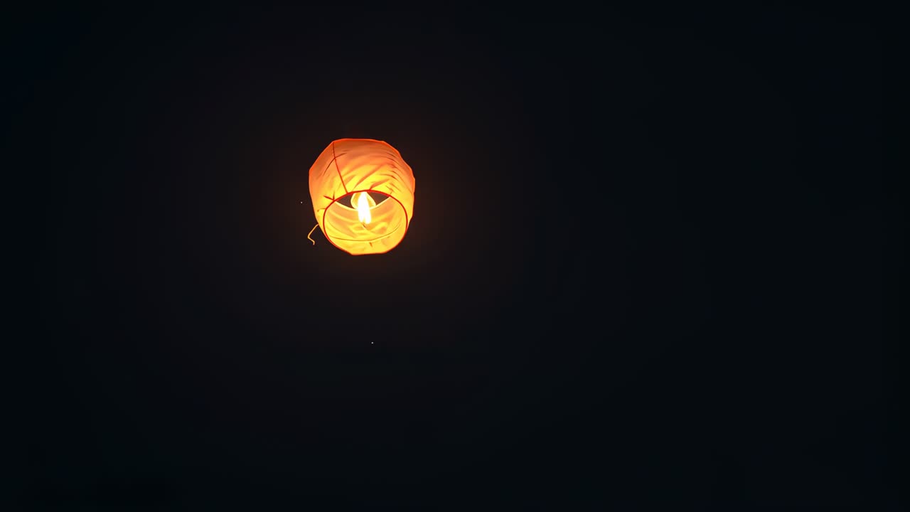 Internal flame igniting lifting orange paper lantern rising and rotating in night sky