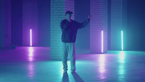 a steel man dances hip-hop freestyle in a modern style in a hall with neon light in purple blue colors. male professional hip hop dancer