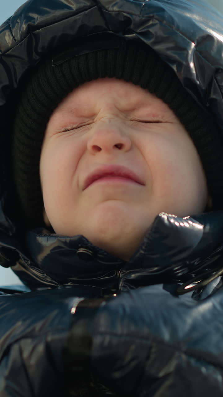 반이는 검은색 재을 입은 어린 아이의 클로즈업, 후드와 베니를 입고, 눈을 천천히 열면서 약간 좌절하고 눈을 히고 있습니다.