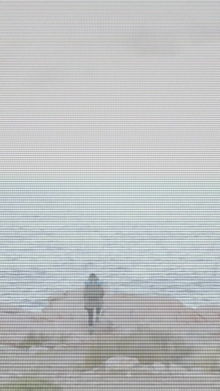 Video verticale: Donna che cammina verso il mare su una costa rocciosa in cerca di una vista, generando nebbia animata per un film