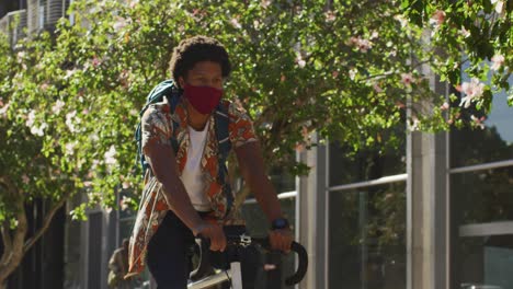 african american man in city, wearing face mask riding bicycle in street