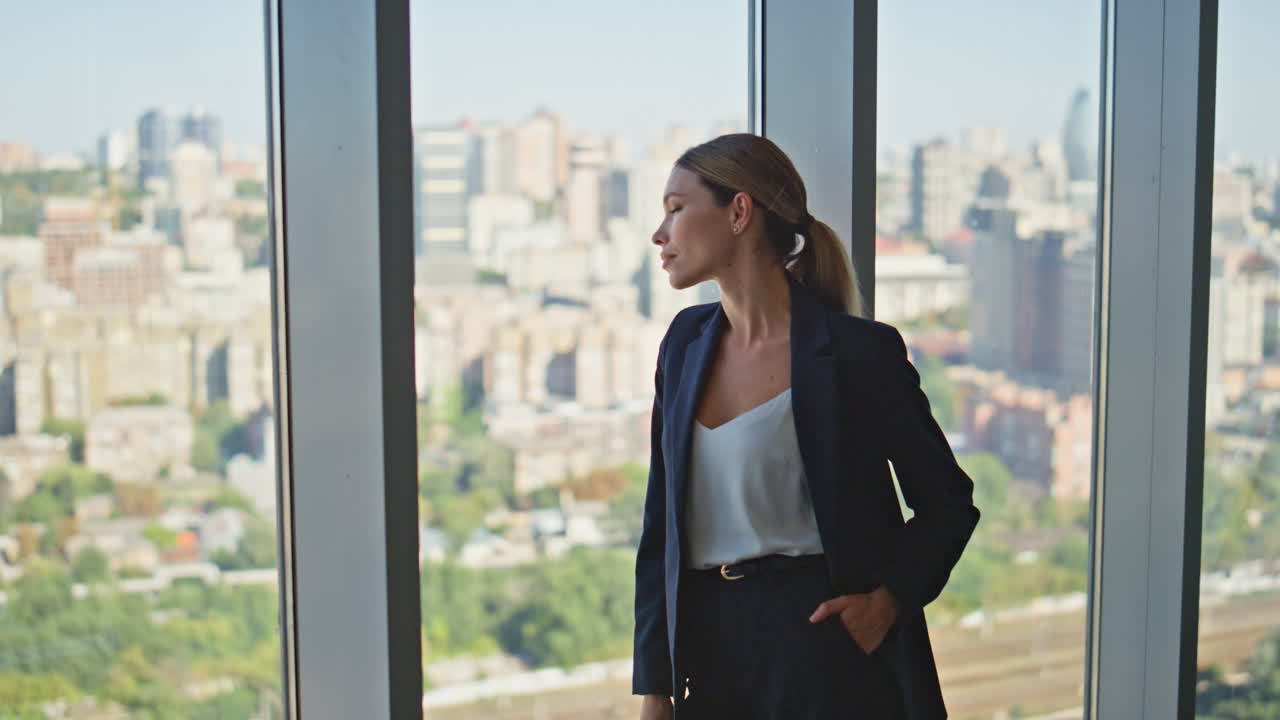 una mujer segura mira por la ventana panorámica. una joven mujer de negocios elegante tomando un descanso.