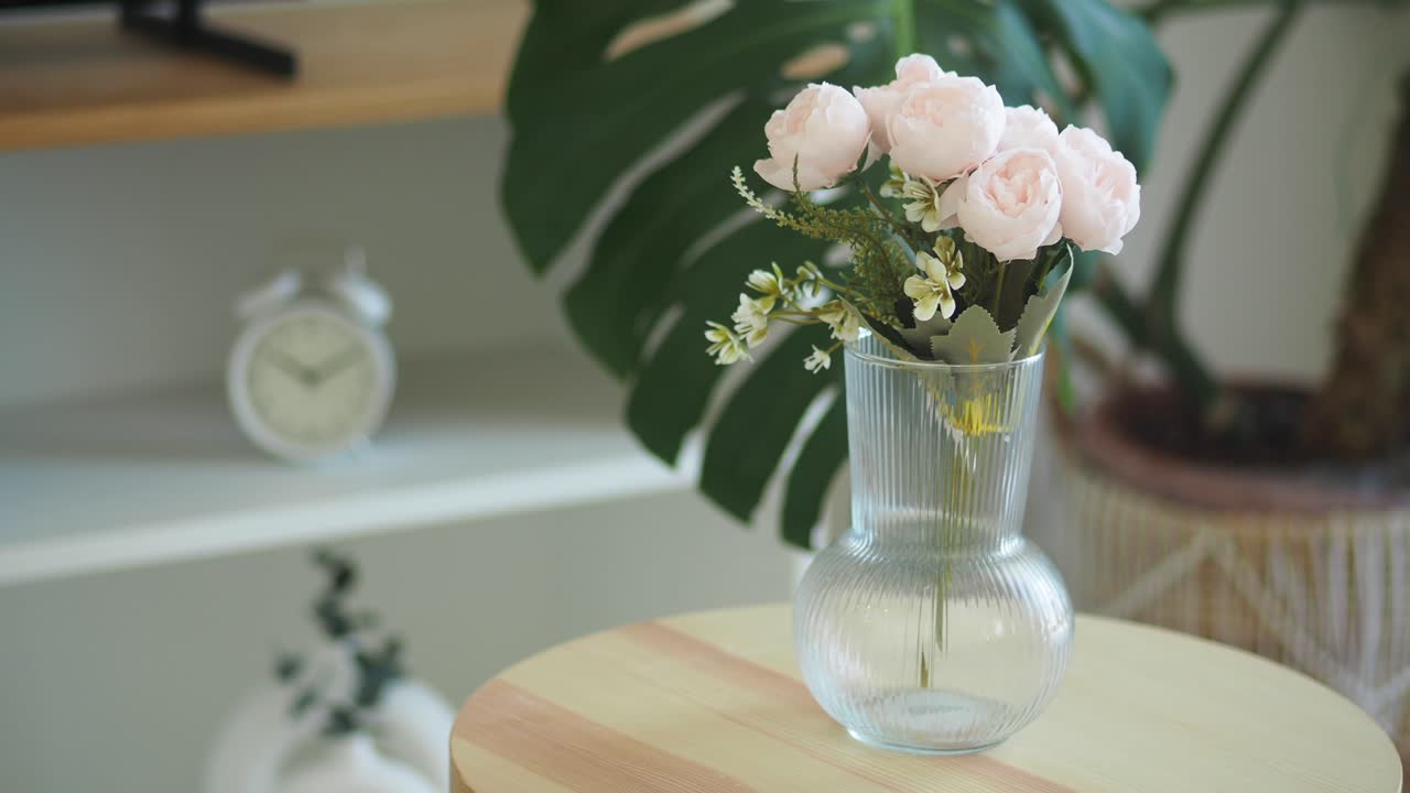 A vase of light pink artificial flowers on a table in an indoor setting