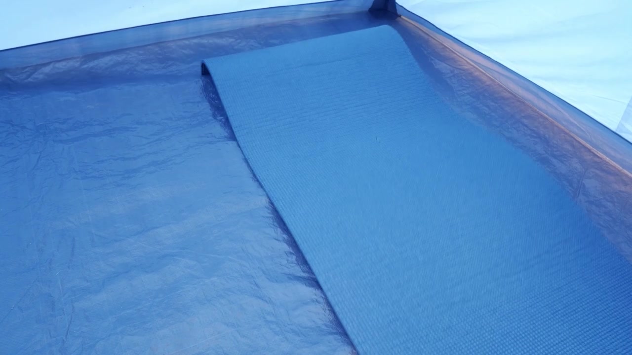 Person unrolling a sleeping pad on tent floor for campsite setup or preparation