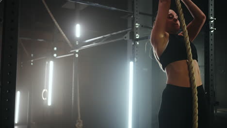 sporty-young-woman-in-black-sportswear-is-jumping-on-rope-and-hanging-in-gym-hall