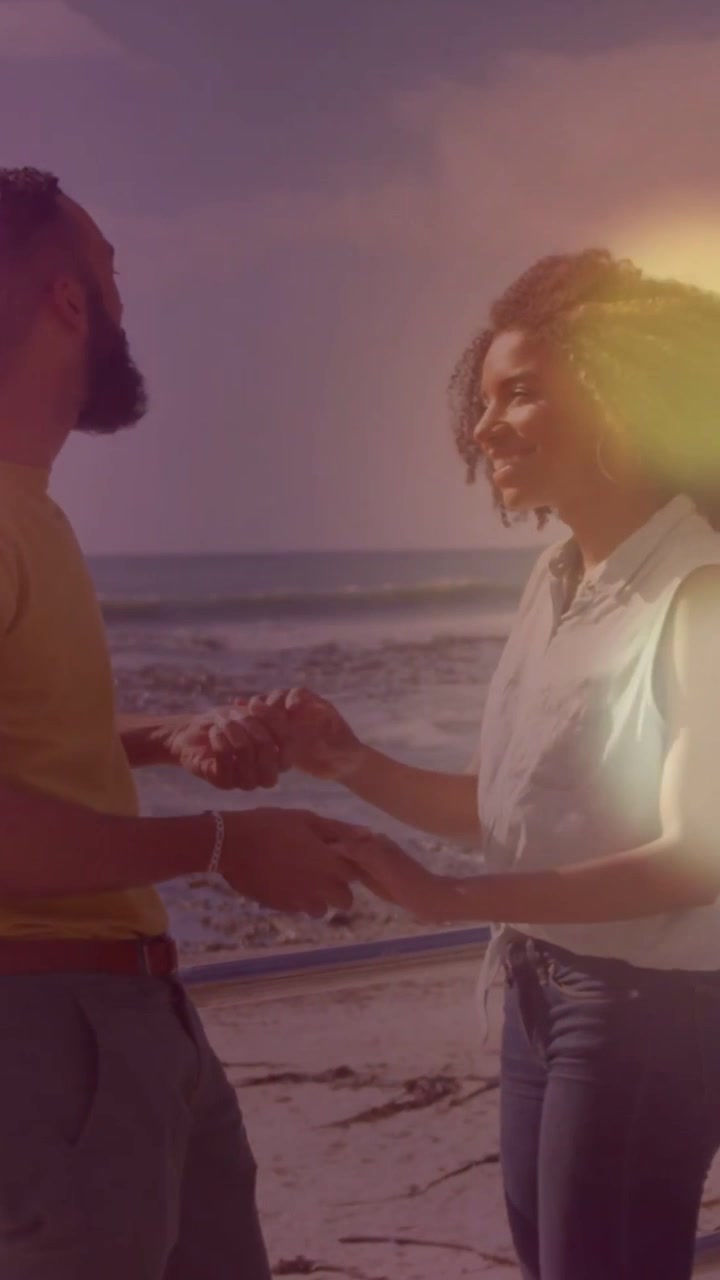 Holding hands, woman in white top and jeans, man in tee smiling at railing with flare
