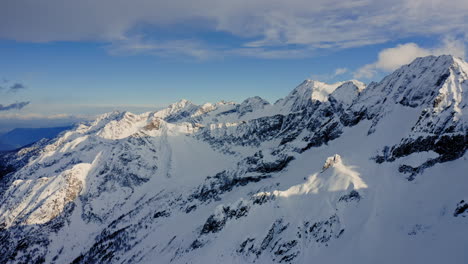 Flying-over-the-Snowy-Mountains-during-Sunny-Day,-Clear-Blue-Sky-and-Fast-Moving-Clouds