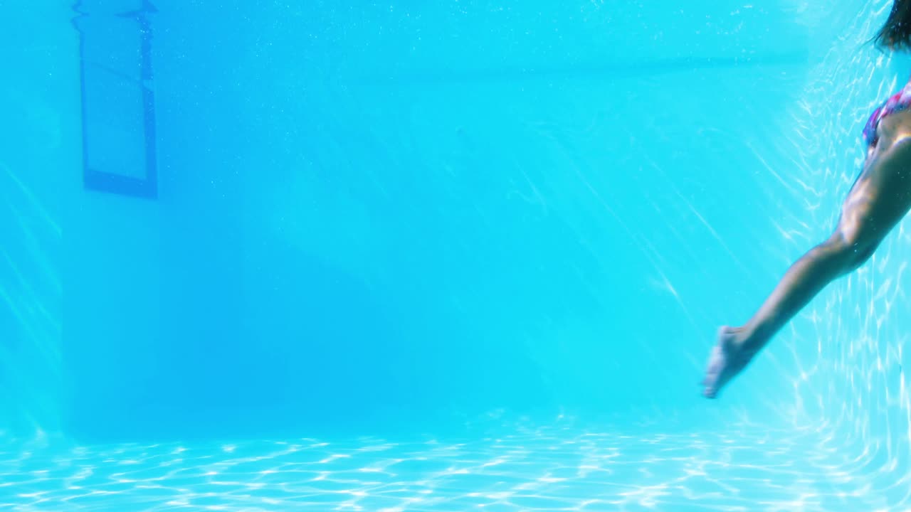 Wanita berambut cokelat cantik berenang di bawah air di kolam renang