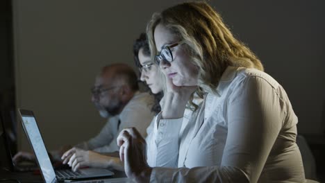 tired colleagues working with laptops in dark office