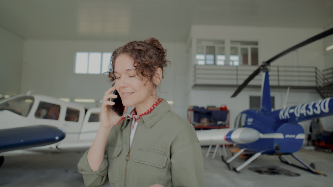 Female Aircraft Mechanic Talking on Phone as Walking through Hangar