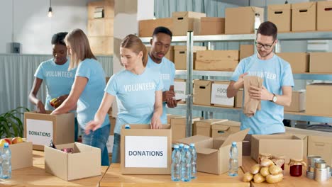 multiethnic group of volunteers packing boxes with food and clothes in charity warehouse