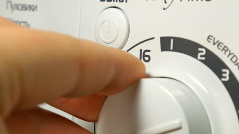 una mano masculina configurando y encendiendo una lavadora electrónica de gama alta.