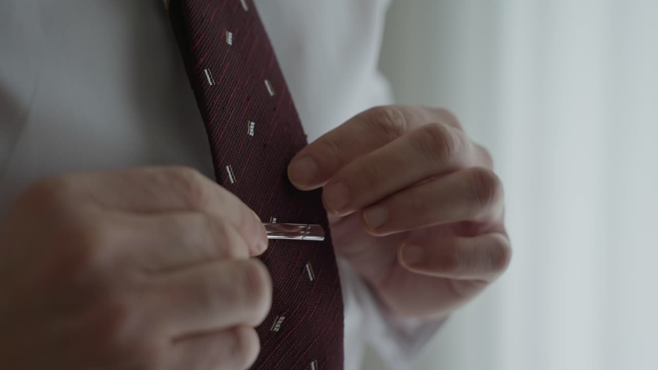Close up tangan sedang memasang batang dasi pada dasi burgundy di atas kemeja putih