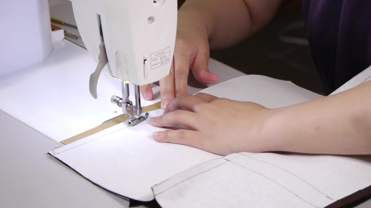 manos empujando tela blanca a través de la máquina de coser para coser el borde exterior