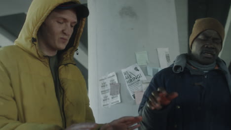 men huddling under an underpass with job posters in winter