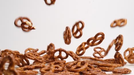 Salty-twisted-pretzel-snack-crackers-falling-onto-white-table-top-and-bouncing-around-into-a-pile-in-slow-motion