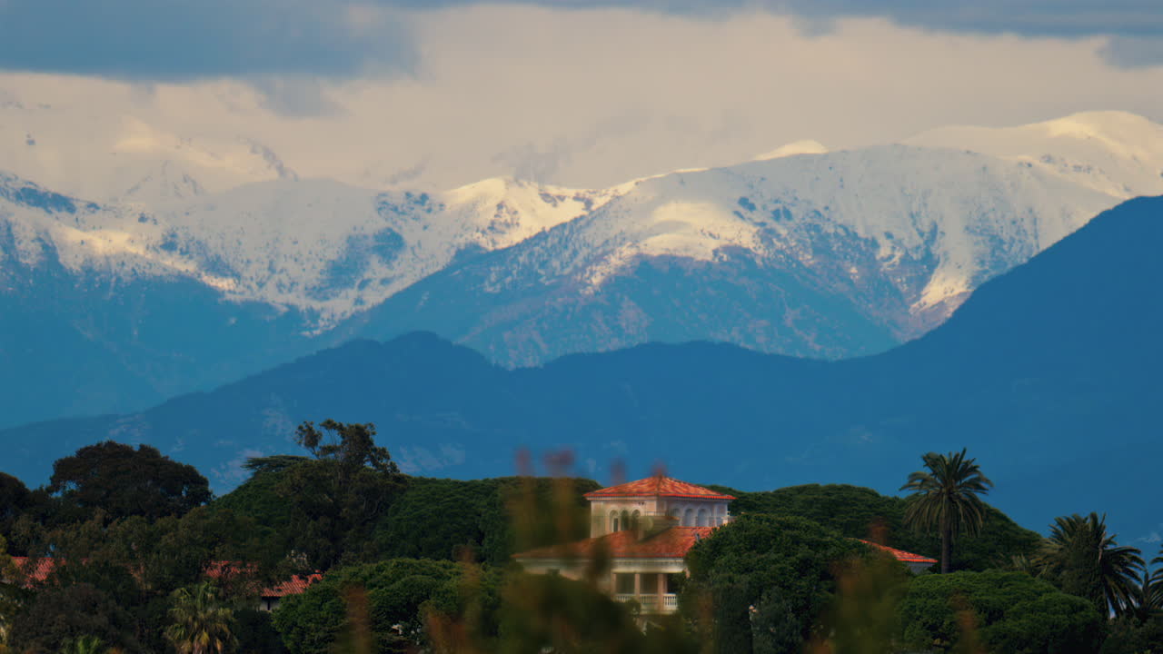 Distant view of orange villas surrounded by green trees with the mountains on the background on a cloudy day