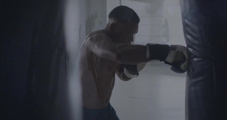 Pugile che entra in palestra e sferra jab e ganci a un sacco da boxe per la salute, con un effetto glitch in sovrapposizione.