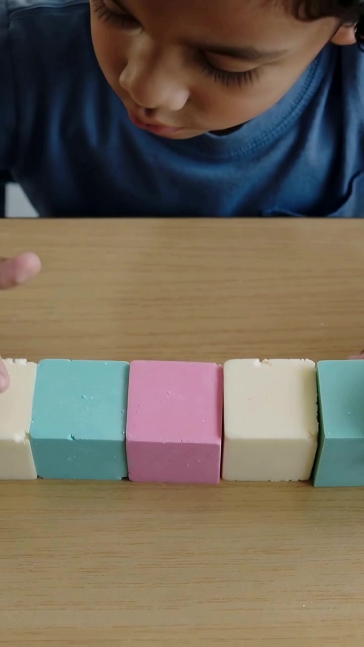 Video vertical: Niño con camiseta azul tocando cinco bloques pastel sobre una mesa de madera, alineándolos