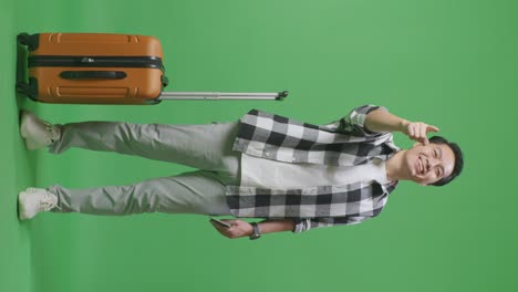 full body of asian male traveler with luggage and passport smiling and touching his chest then pointing at you while standing in the green screen background studio