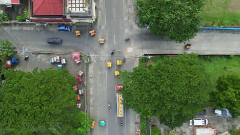 Vista-Aérea-De-Arriba-Hacia-Abajo-De-Camiones-De-Carga-Y-Triciclos-Conduciendo-Por-Calles-Rurales-Provinciales-E-Intersecciones-En-Una-Pintoresca-Ciudad-Filipina