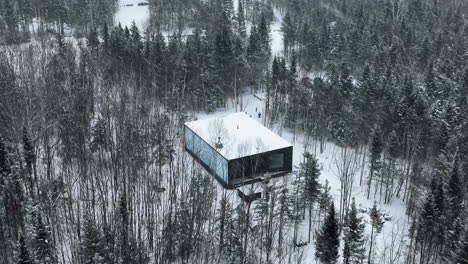 Volando-Por-Encima-De-La-Cabina-Reflejada-En-El-Bosque-Invernal-En-Charlevoix,-Quebec,-Canadá