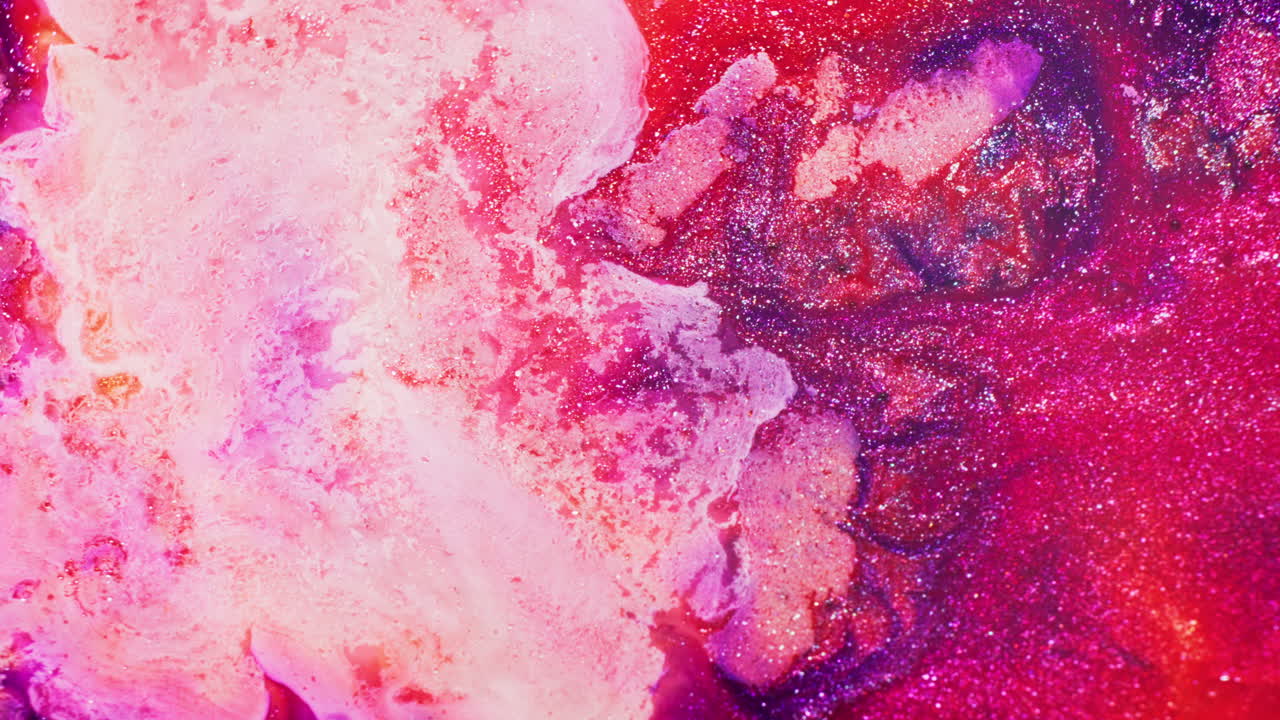Macro shot of orange, red, pink, and purple glitter ink reacting to injected air, creating dynamic swirling and shifting movement