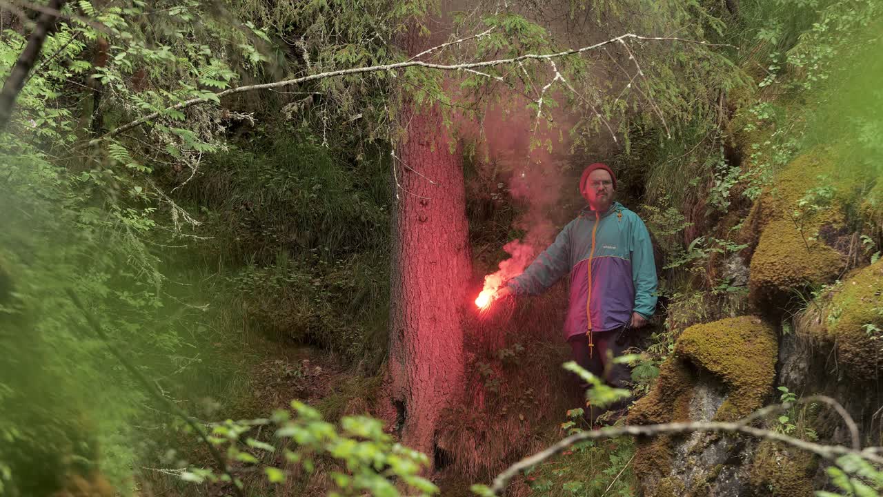 hombre con señal de humo rojo en el bosque
