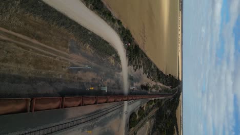 vertical drone flight over old cargo train transporting goods between golden wheat fields in australia