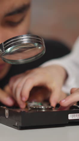 asian technician with curious little schoolgirl examines open hard disk drive details in casing sitting at table in laboratory extreme closeup