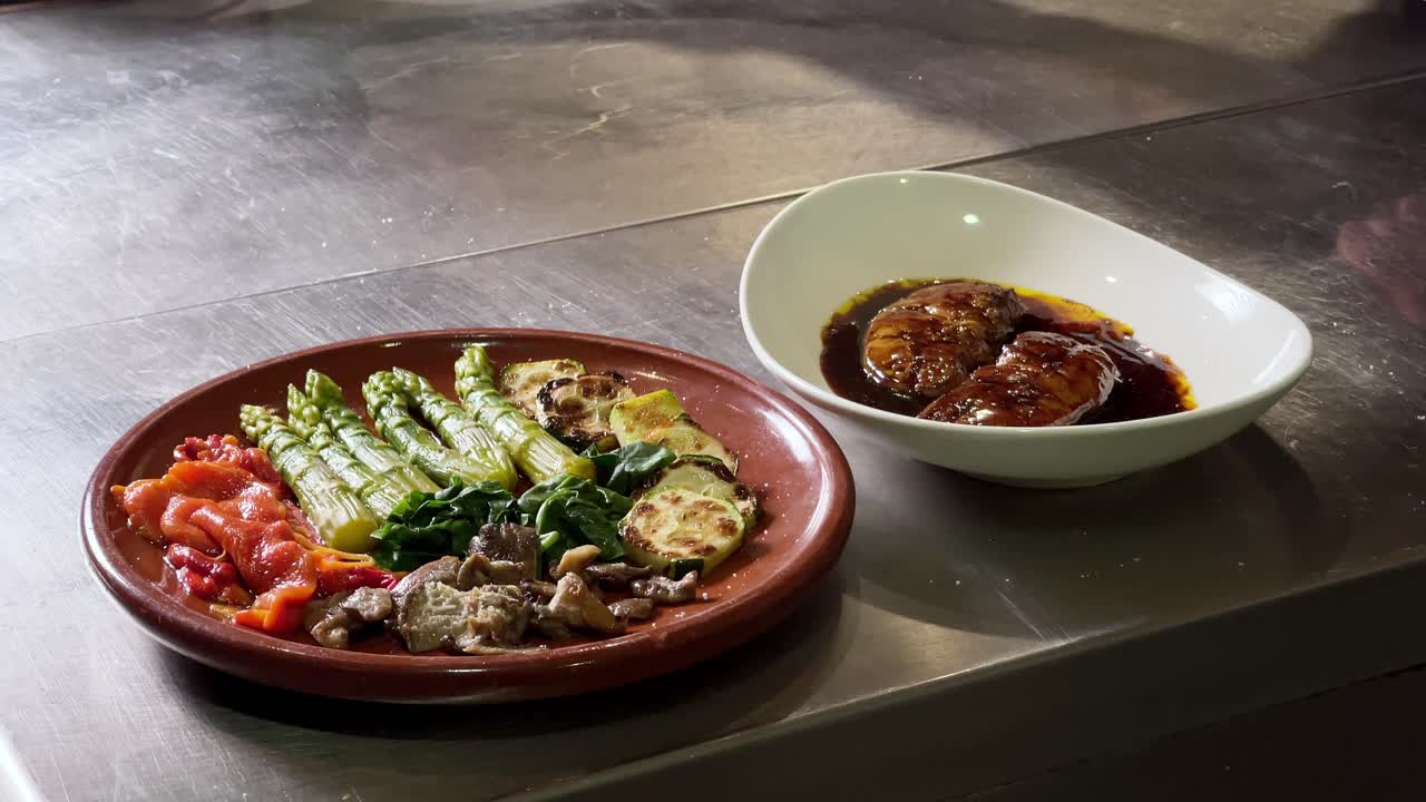 요리사는 튀긴 생선 요리를 카메라에 넣고 꺼내는 반면 그린 샐러드와 푸아그라는 레스토랑 주방의 카운터에 있습니다.