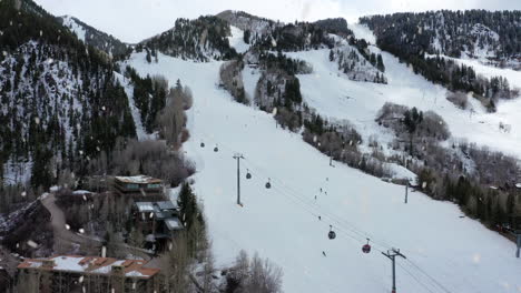 majestic ski track slope with cable cars during snowfall, aerial ascend view