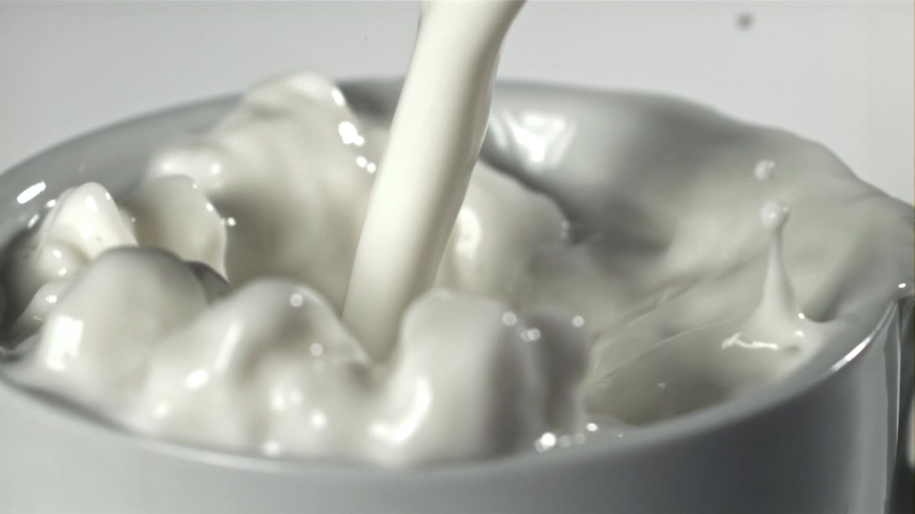 白いカップに牛乳が注がれるスローモーションのクローズアップ