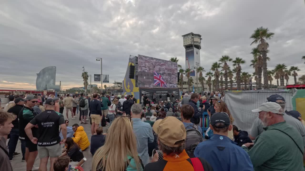 Crowd outside watching the 37th America´s cup on a giant screen. The Vela hotel appears in the background of the image.