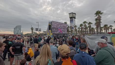 crowd outside watching the 37th america´s cup on a giant screen. the vela hotel appears in the background of the image.