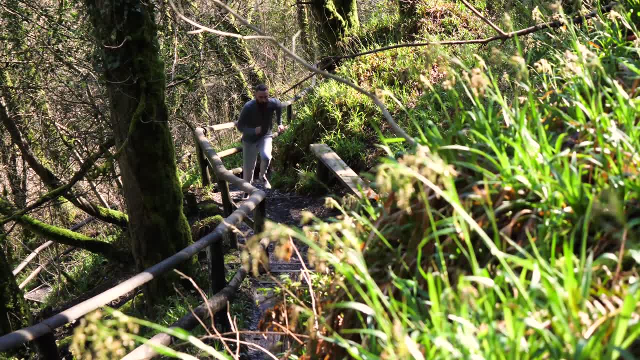 슬로우 모션 수염을 기른 젊은 남자가 조각된 숲길을 달리고 있다