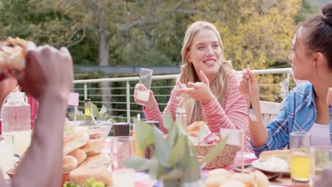 happy diverse group of friends eating and talking at dinner table in garden, slow motion