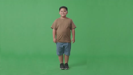 cuerpo lleno de niño asiático sonriendo cálidamente en el fondo de la pantalla verde en el estudio
