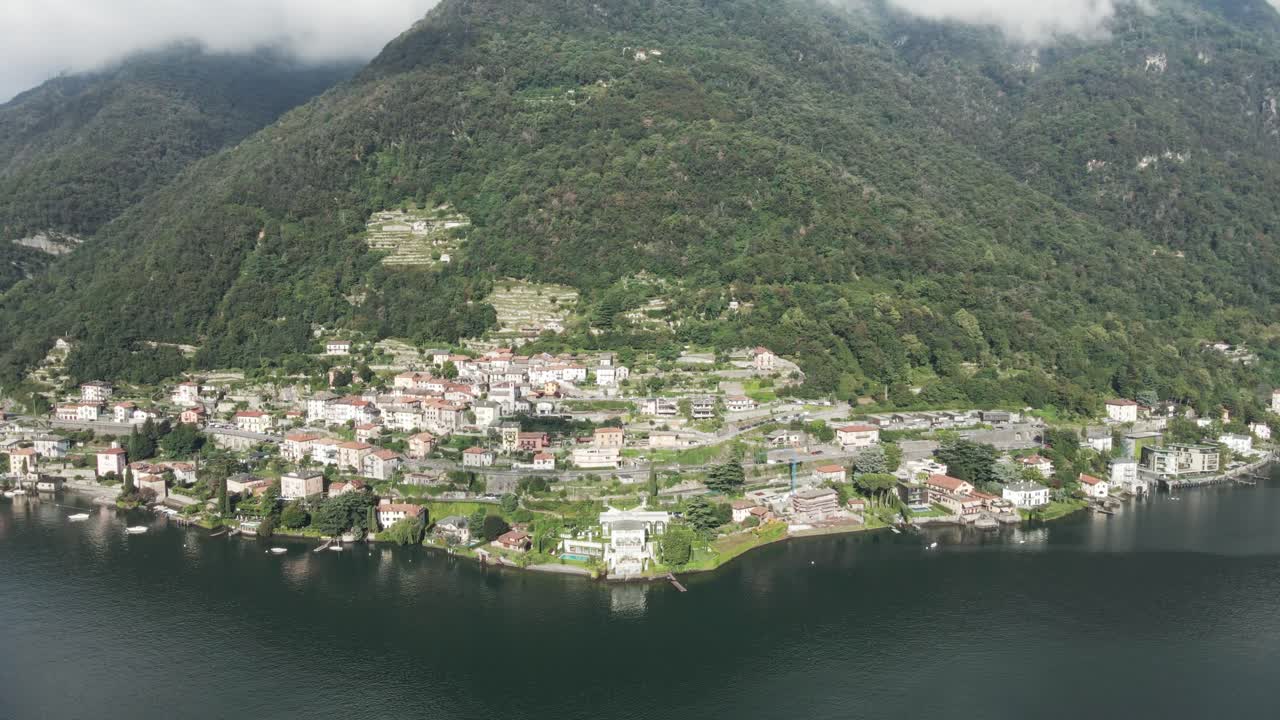 이탈리아의 코모 호수 연안에 있는 무거운 구름 인 산 아래의 유명한 빌라를 찍은 기울어지는 드론