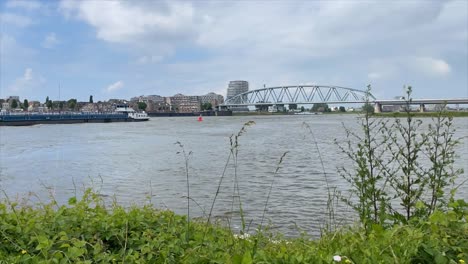 Timelapse-of-The-Nijmegen-railway-bridge-in-the-background-on-River-Waal-connecting-the-city-of-Nijmegen-to-the-town-of-Lent-in-the-Netherlands,-Europe