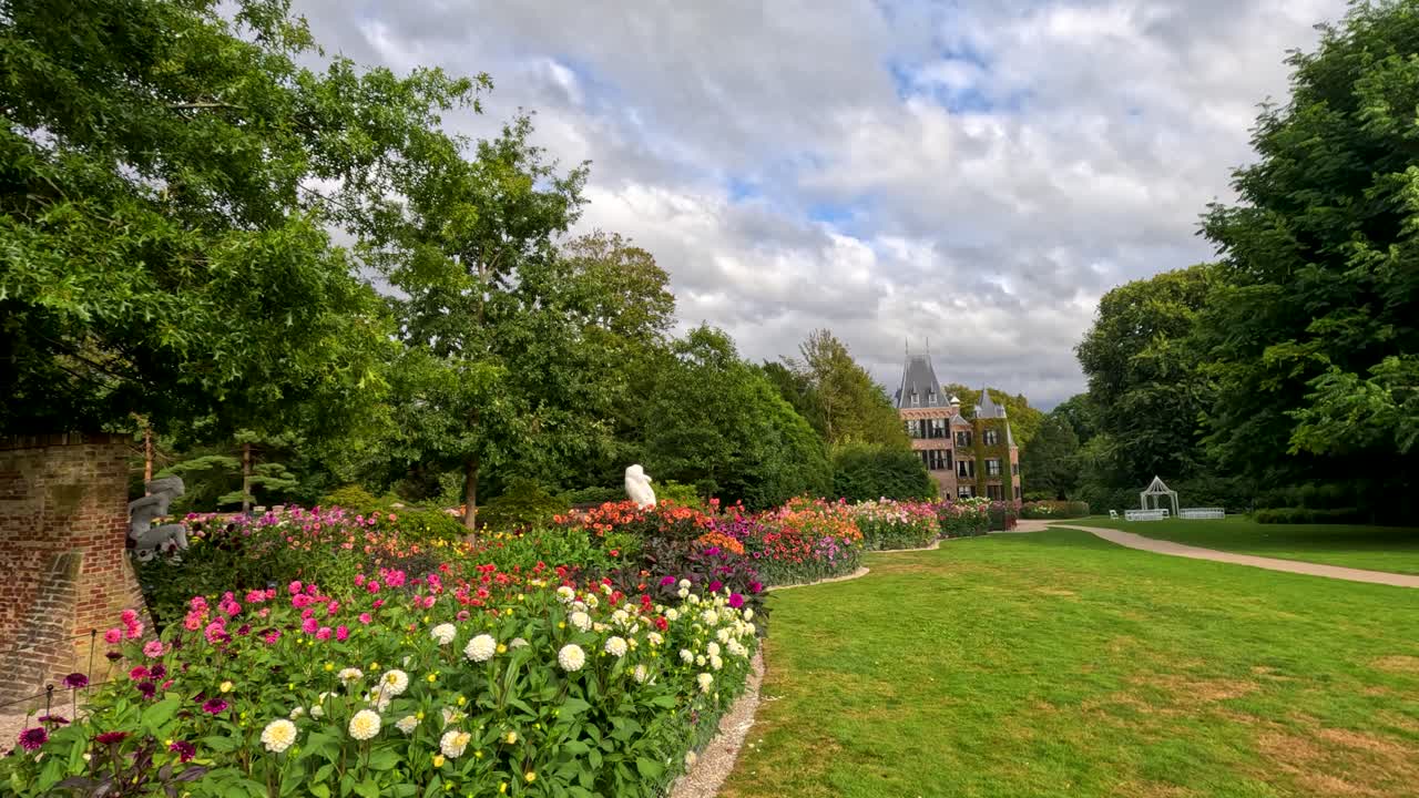 Camera glides past colorful dahlia beds and brick walls, revealing a distant castle in daylight