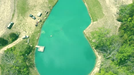 4k aerial footage ascending above a beautiful blue lake to expose tree line, vehicles and a deck