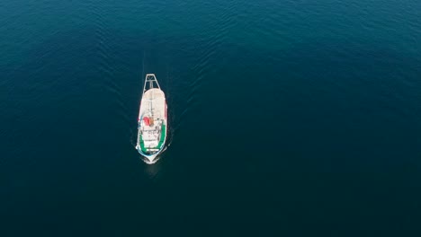 Vista-Aérea-De-Arriba-Hacia-Abajo-Del-Barco-De-Pesca-Navegando-En-Un-Mar-Azul-Profundo,-Día-Soleado