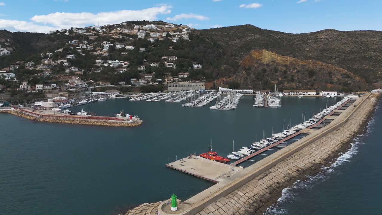 Curved dock formation hugs coastline with boats moored and hills beyond