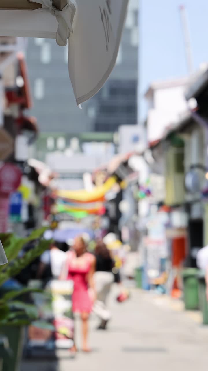 色鮮やかな街路を散策する歩行者たち。明るい真昼の日差し、浅い被写界深度、手持ちカメラで撮影。
