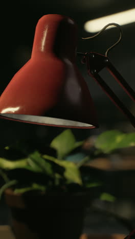 primer plano de una lámpara de escritorio roja con una planta en el fondo