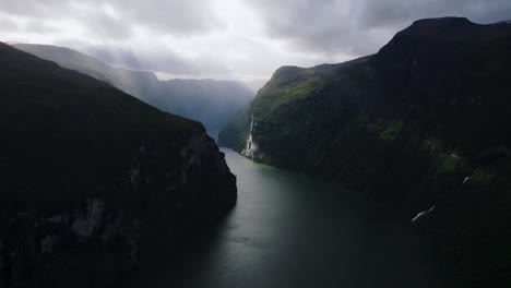 geirangerfjord, norway. aerial revealing famous fjord, layered mountains, clouds, sun and deep water