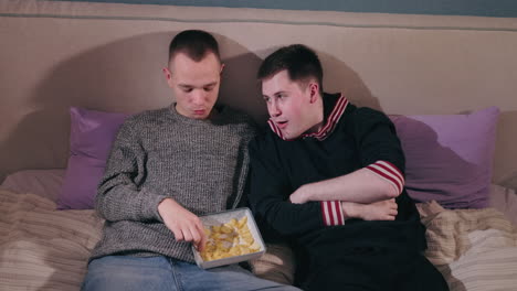 two friends enjoying snacks on a bed