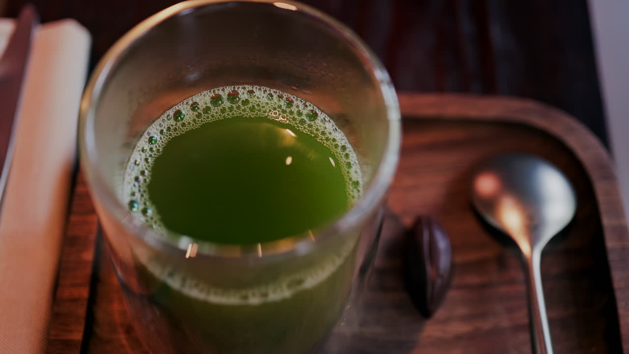 Primer plano de un vaso de té verde sobre una bandeja de madera en una mesa